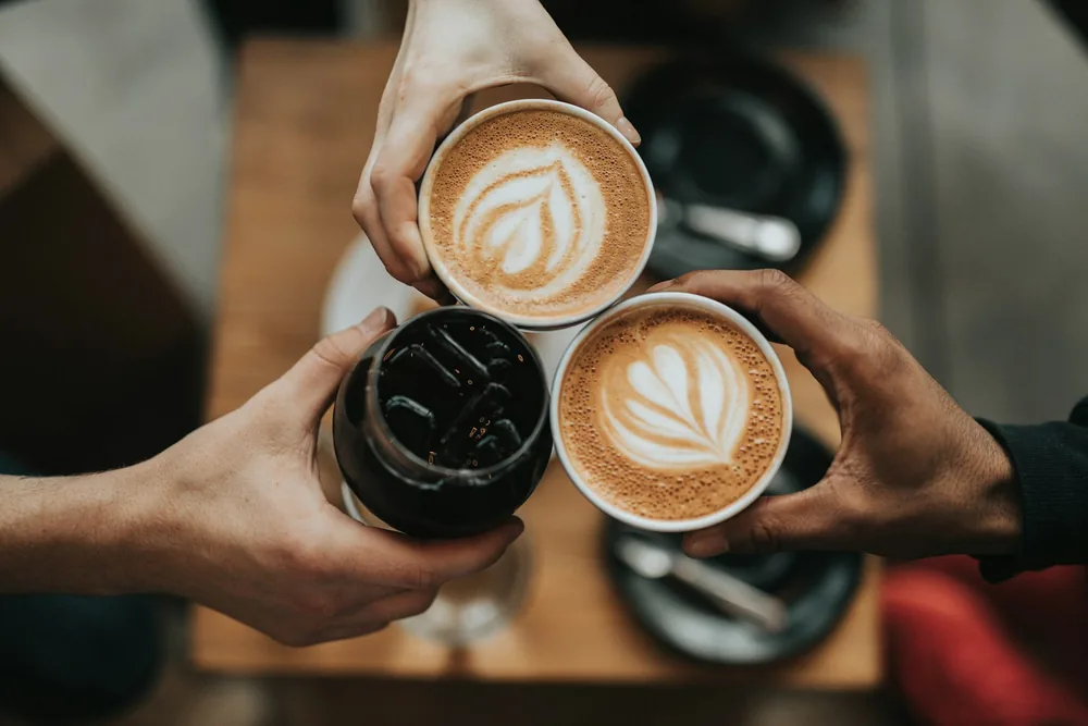 コーヒーを持ち寄って乾杯する3人の手元